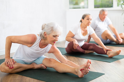 Senior visitor of yoga class engaged Pilates in sports studio hall. Elderly woman stretches.