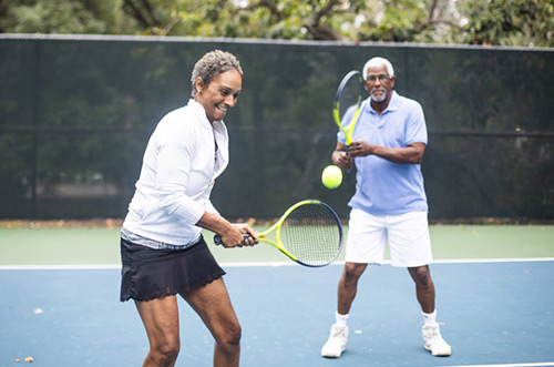 A Senior Black Couple Playing Doubles Tennis on a cloudy morning